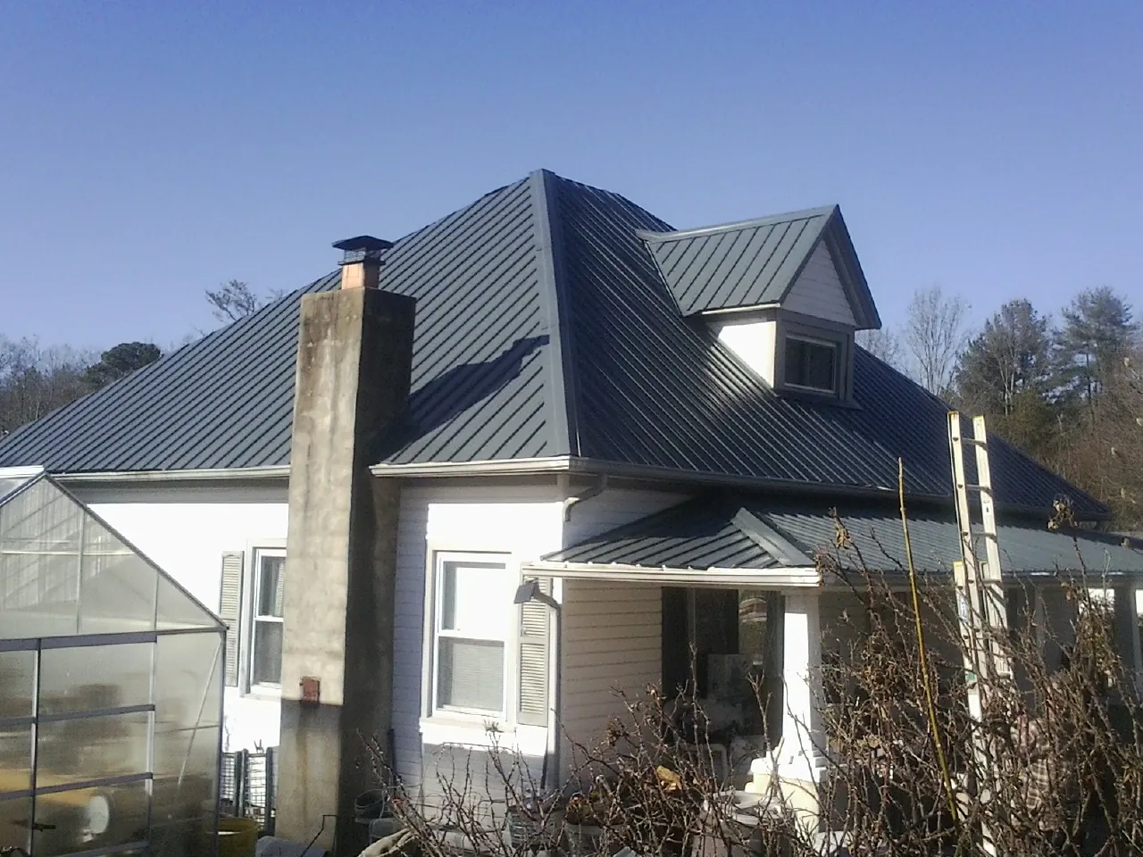 Dark blue standing seam metal roof on a white farmhouse with dormer — Slate & Tile Roof Repair by Roofing Brothers in Liberal
