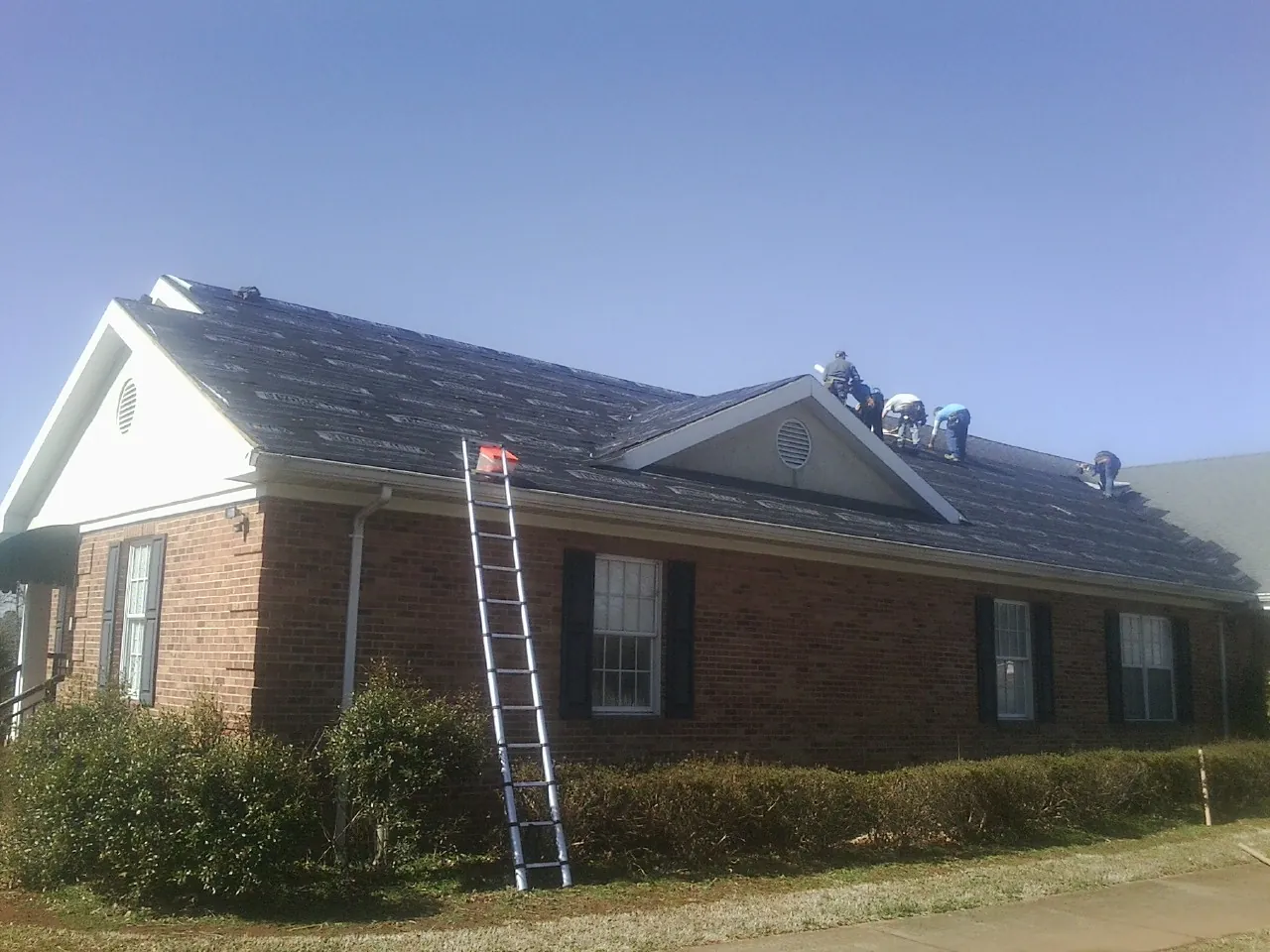 Crew tearing shingles off a brick ranch roof with a ladder set — Metal Roof Repair work by our crew in Liberal