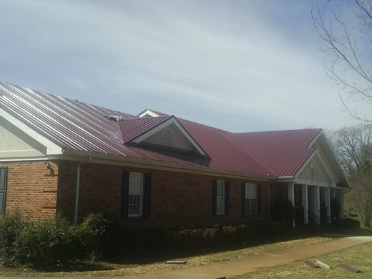 Red metal roof with gabled entries on a long brick building, from a Hail Damage Roof Repair job in Liberal