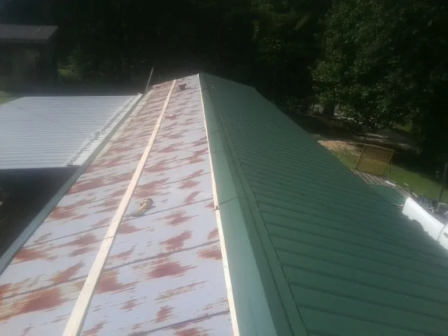 Old rusted panels beside newly installed green metal roofing — Wind Damage Roof Repair by Roofing Brothers in Liberal