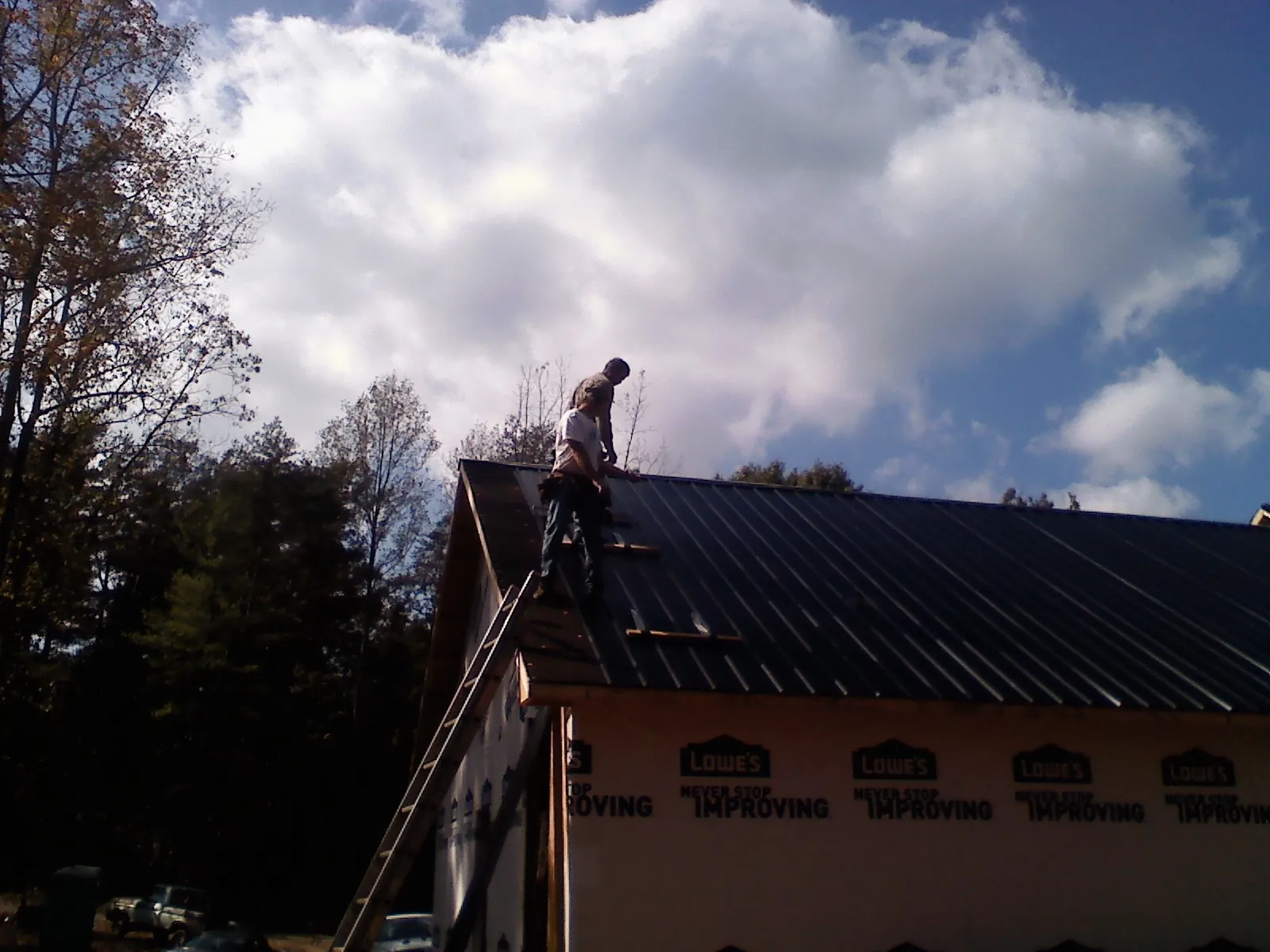 Roofer fastening dark metal panels high against a cloudy sky, from a Roof Inspection job in Liberal