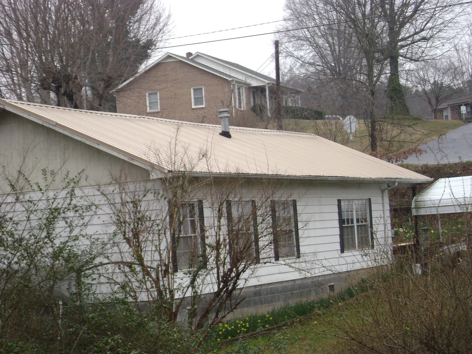 Tan metal roof on a white sided house set into a hillside — Commercial Roofing by Roofing Brothers in Liberal